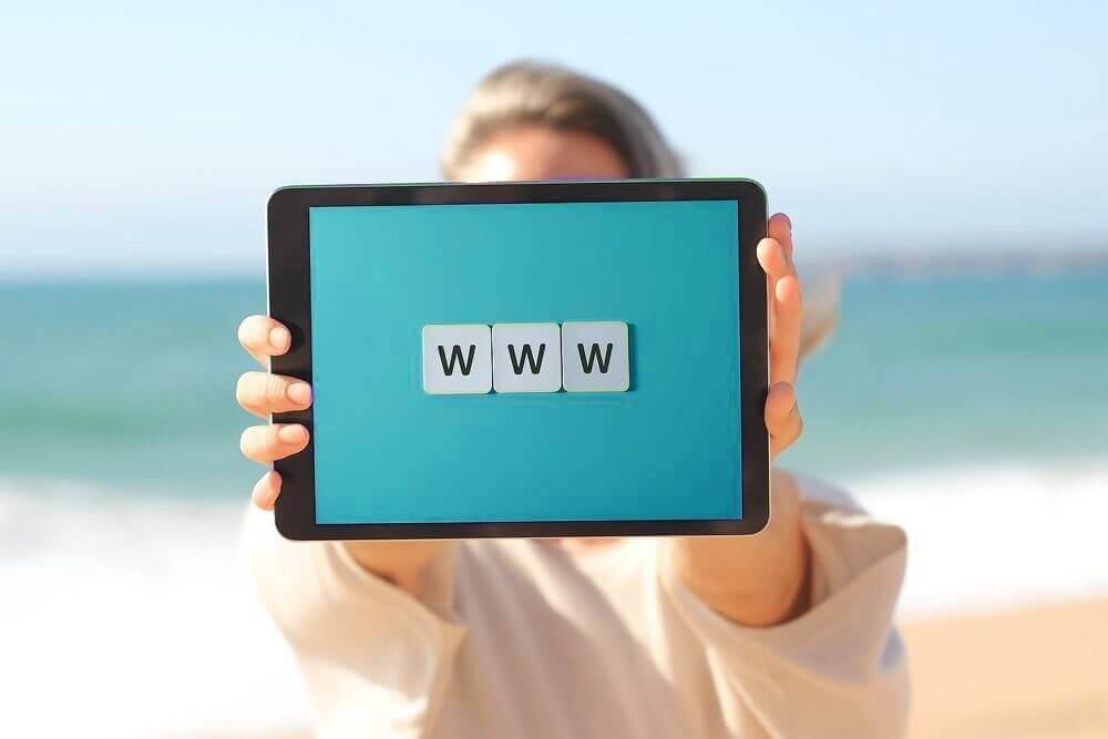 Tablette affichant « www » sur fond turquoise, face à la mer